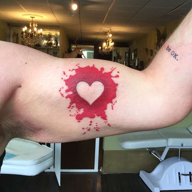 Tatuaje de corazón sobre mancha de color rojo